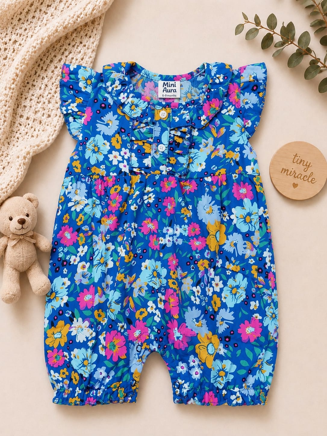 Baby girl royal blue sleeveless romper with vibrant pink and yellow floral print and ruffle collar.