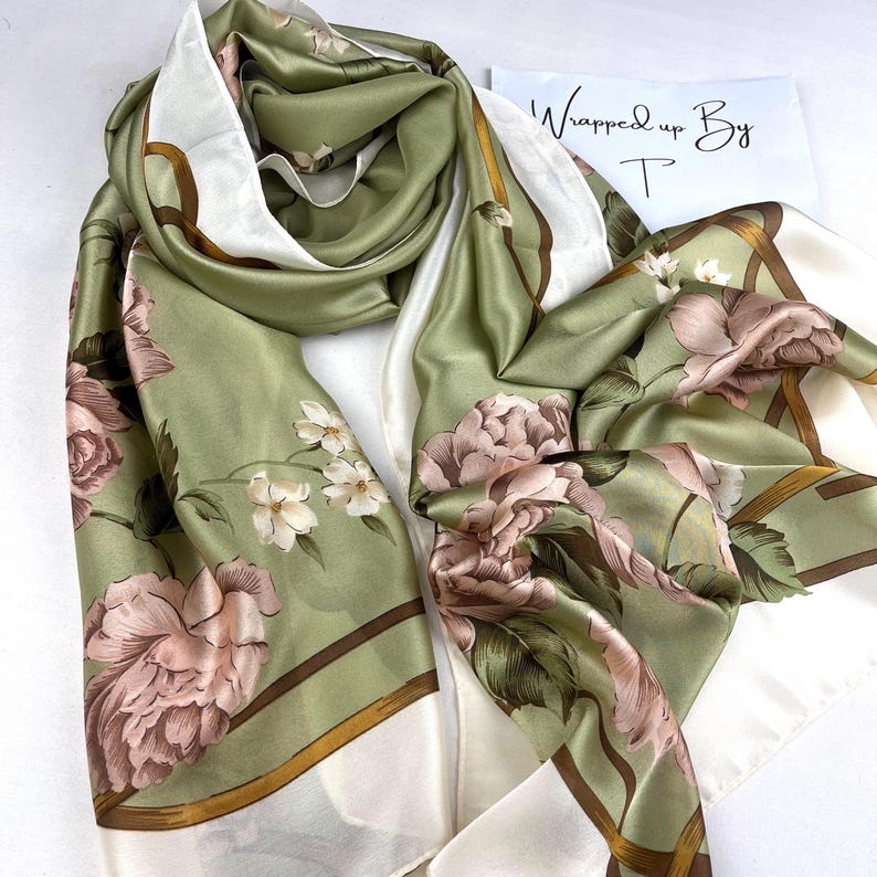 Sage green silk-satin scarf featuring large blush pink peonies and small white flowers with a gold and white bordered edge