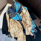 Luxury silk-satin scarf featuring a repeating gold interlocking chain motif on navy blue, teal, and champagne panels