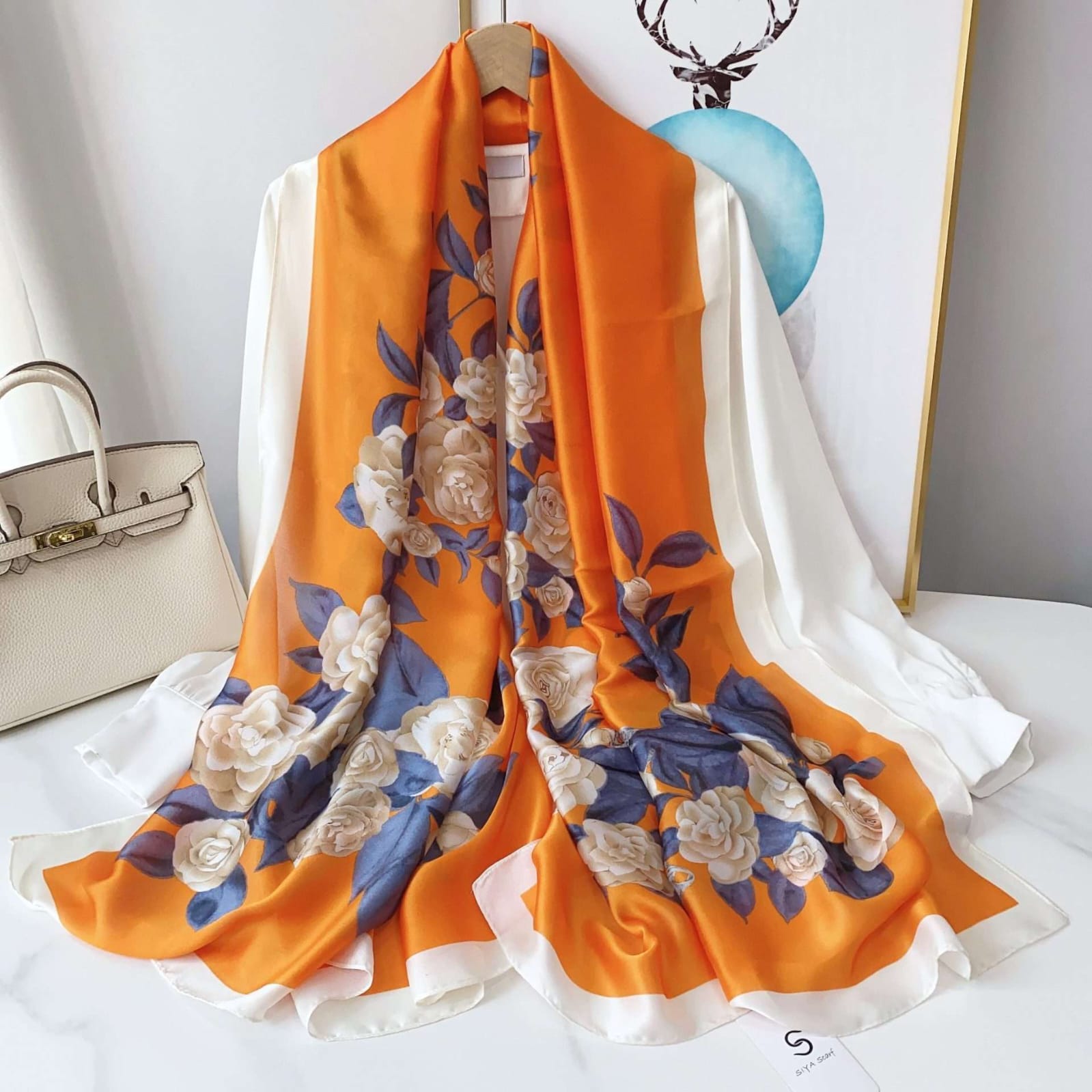 Vibrant orange silk-satin scarf featuring a large cream rose floral print with blue-grey leaves and a white bordered edge
