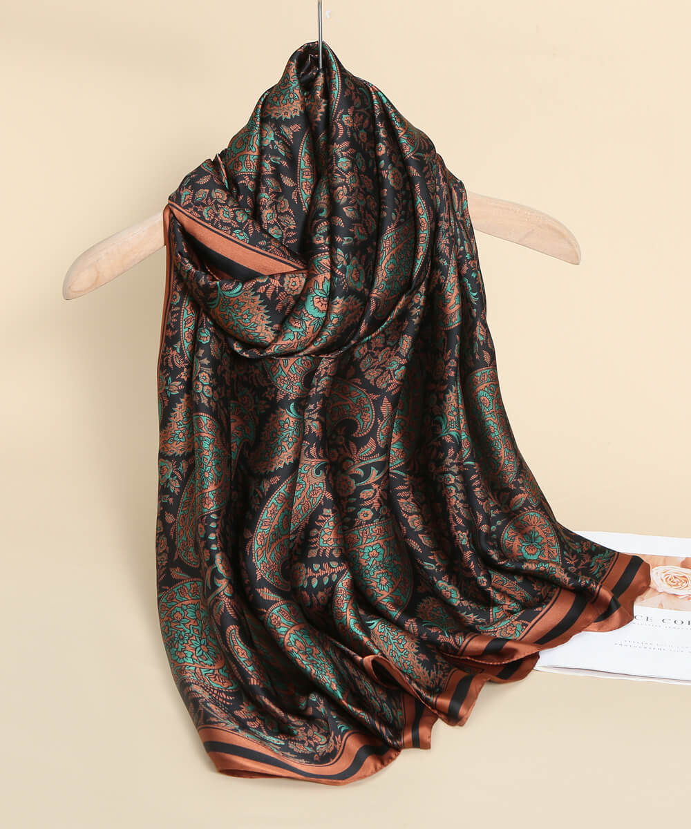 Luxury black silk-satin scarf featuring a detailed emerald green and bronze paisley motif with a bronze bordered edge